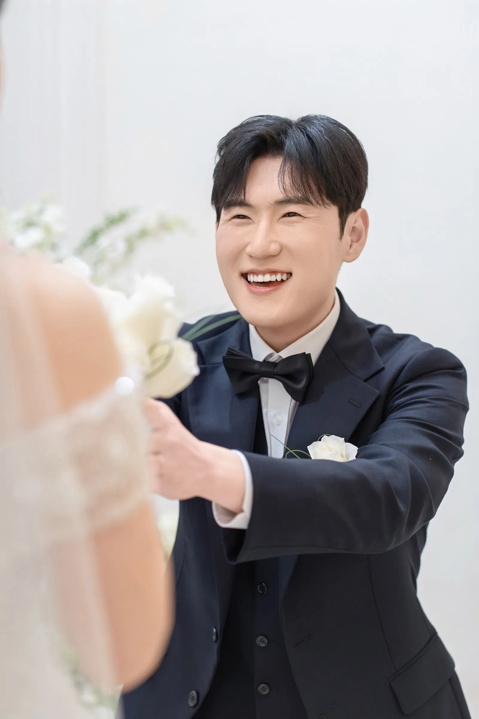신부 쪽으로 흰 장미 부케를 내민 신랑과 흐릿하게 보이는 신부의 뒷모습