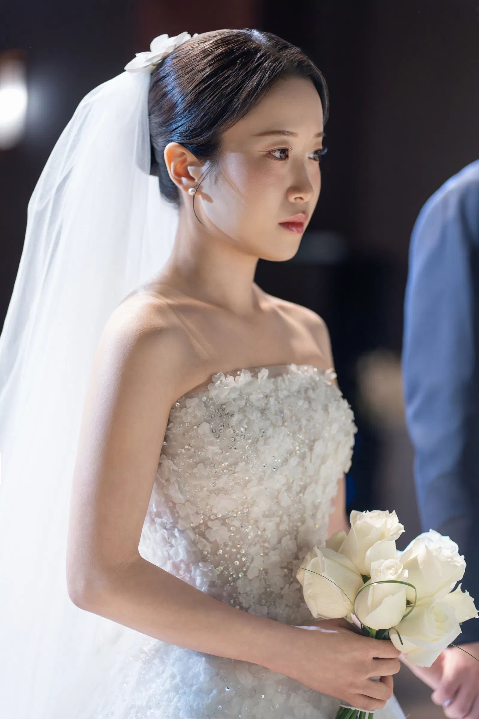 예식대에서 흰 장미 부케를 든 신부와 오른쪽 앞에 보이는 신랑의 팔