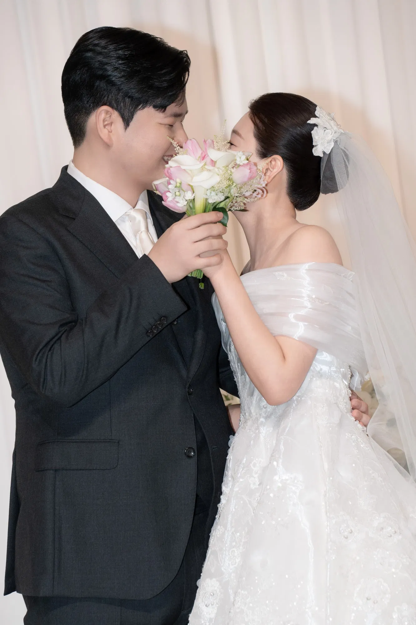 스타시티아트홀에서 분홍빛 부케를 사이에 두고 얼굴을 가까이한 신랑신부